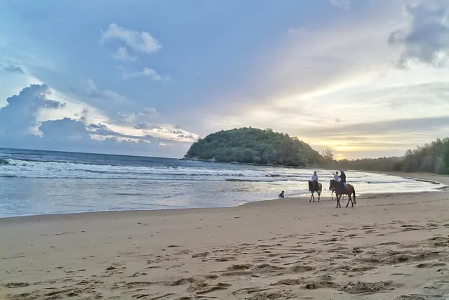 Layan beach at dusk with horse riders and a forested headland behind